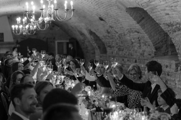 Hochzeitsgesellschaft an einer langen Tafel im Gewölbe unter Kronleuchtern